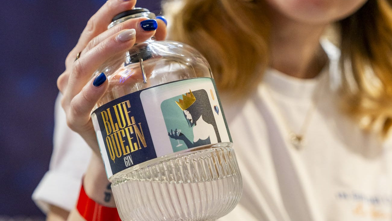 Iulia che tiene in mano in primo piano ravvicinato una bellissima bottiglie di Blue Queen Gin. Si può vedere l'illustrazione della Regina di cuori e la scritta Blue Queen dorata.