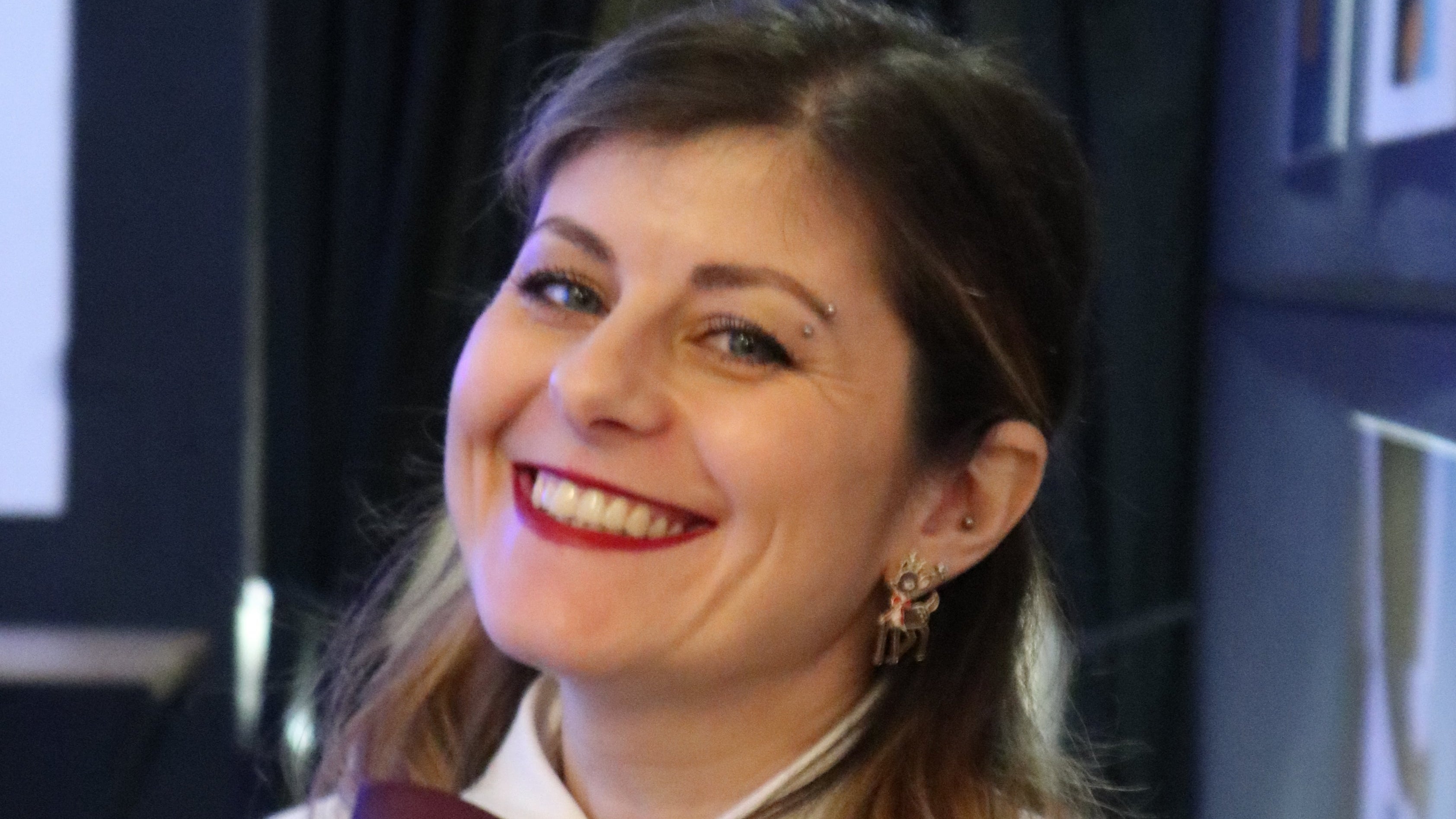 Ritrato a 3 quarti di Iulkia che sorride col suo sorriso caratteristico molto contagioso, occhi blu, rossetto rosso, orecchino a forma di renna piccola